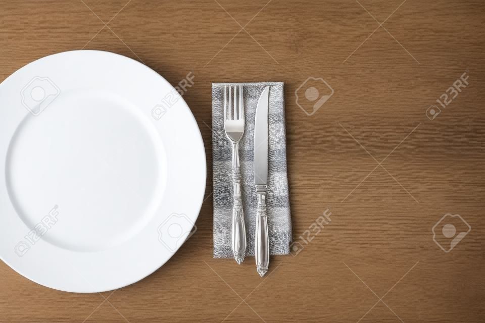 white plate and fork with knife on napkin on wooden table