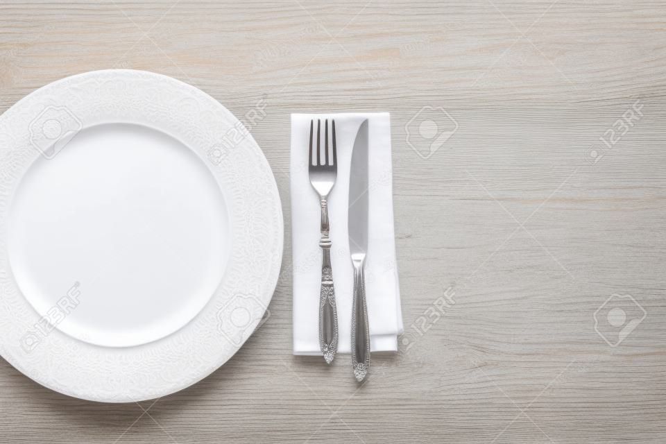 white plate and fork with knife on napkin on wooden table