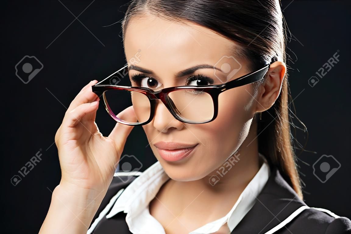 Porträt einer schönen Geschäftsfrau mit Brille, die in die Kamera schaut, isoliert auf schwarz