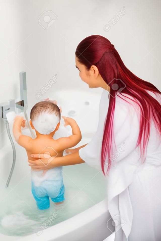 Madre con hijo de lavado de pelo largo en el baño blanco