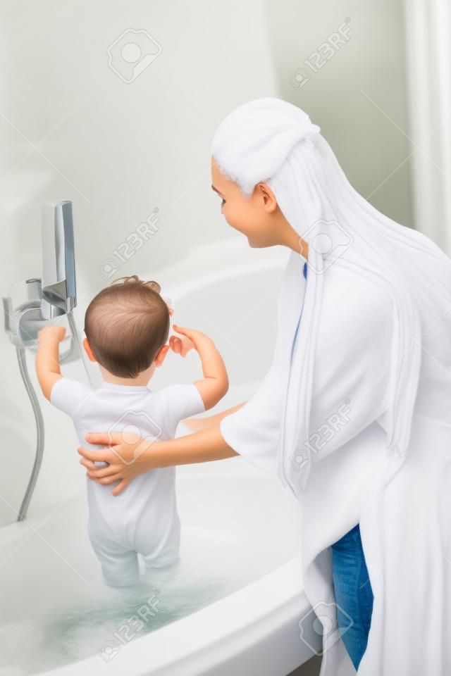 Mère aux cheveux longs lave-fils dans la salle de bain blanche