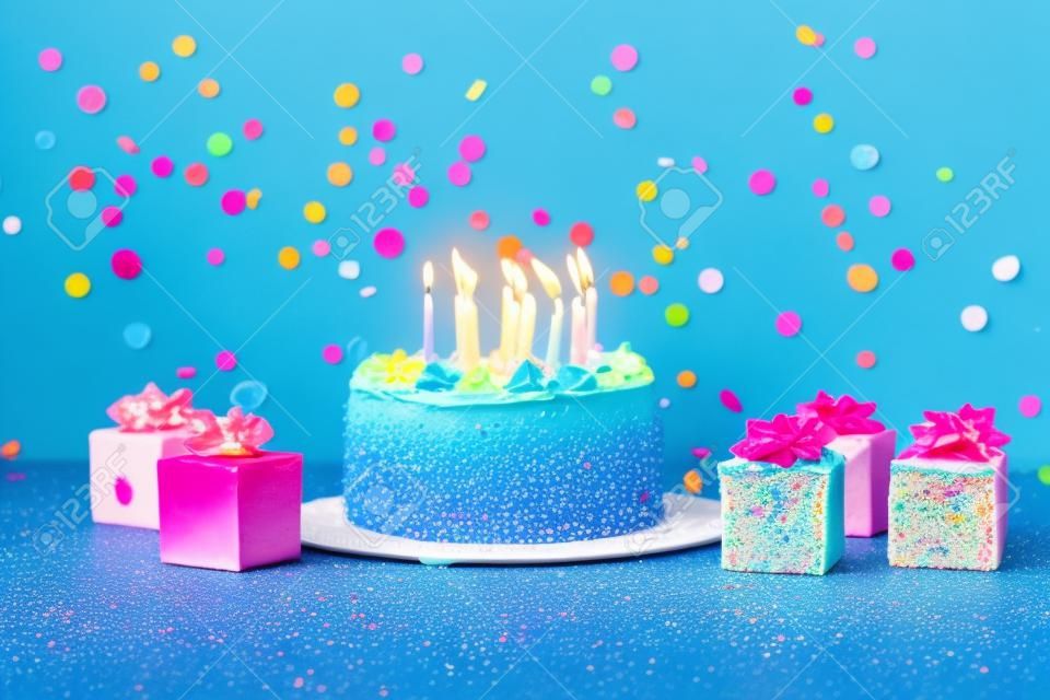 Smakelijke taart met kaarsen, kleurrijke geschenken en confetti op blauwe achtergrond
