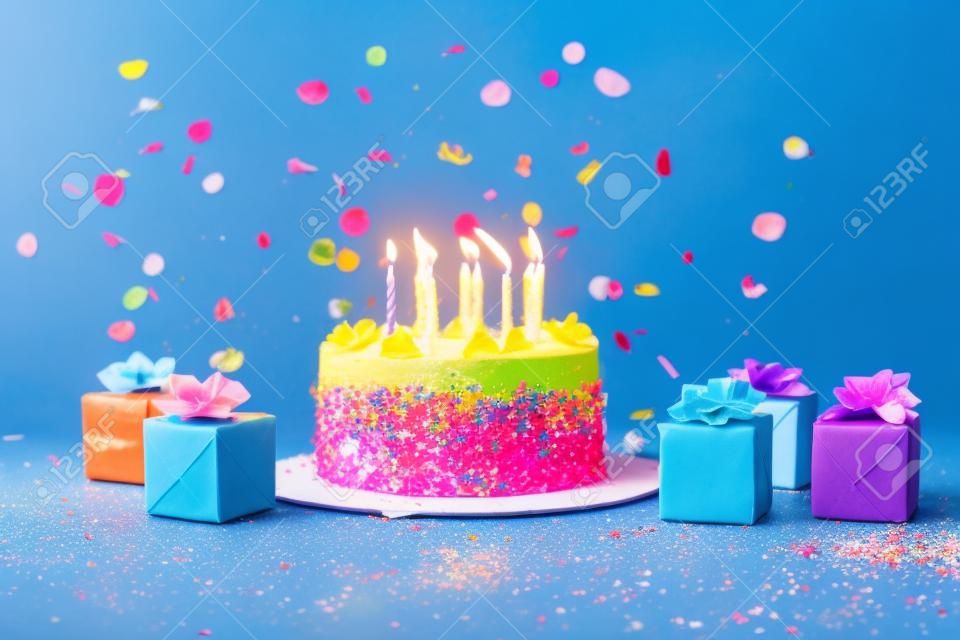 Smakelijke taart met kaarsen, kleurrijke geschenken en confetti op blauwe achtergrond