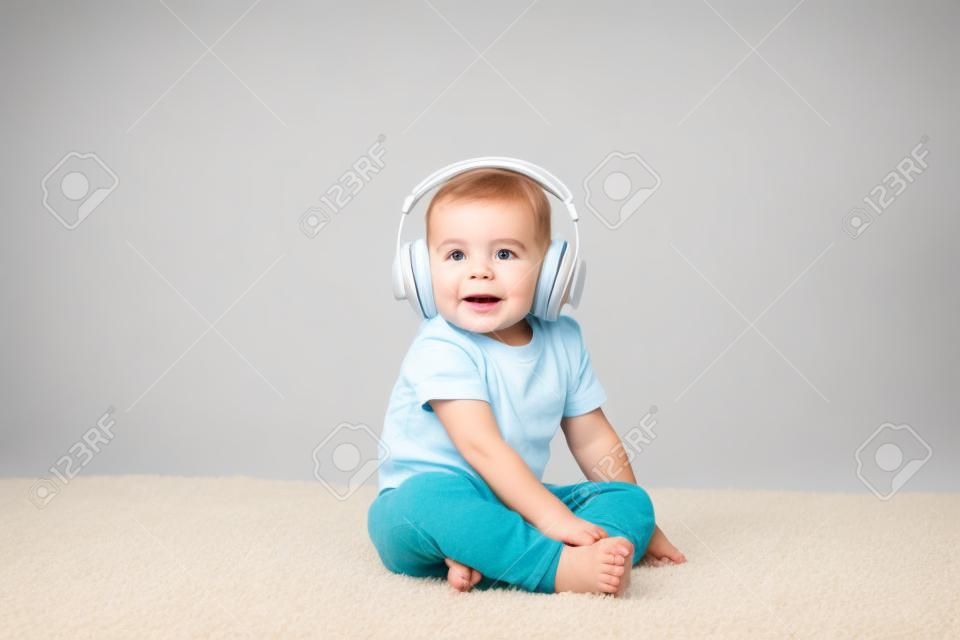 Niño niño sentado sobre una alfombra con auriculares aislado en blanco