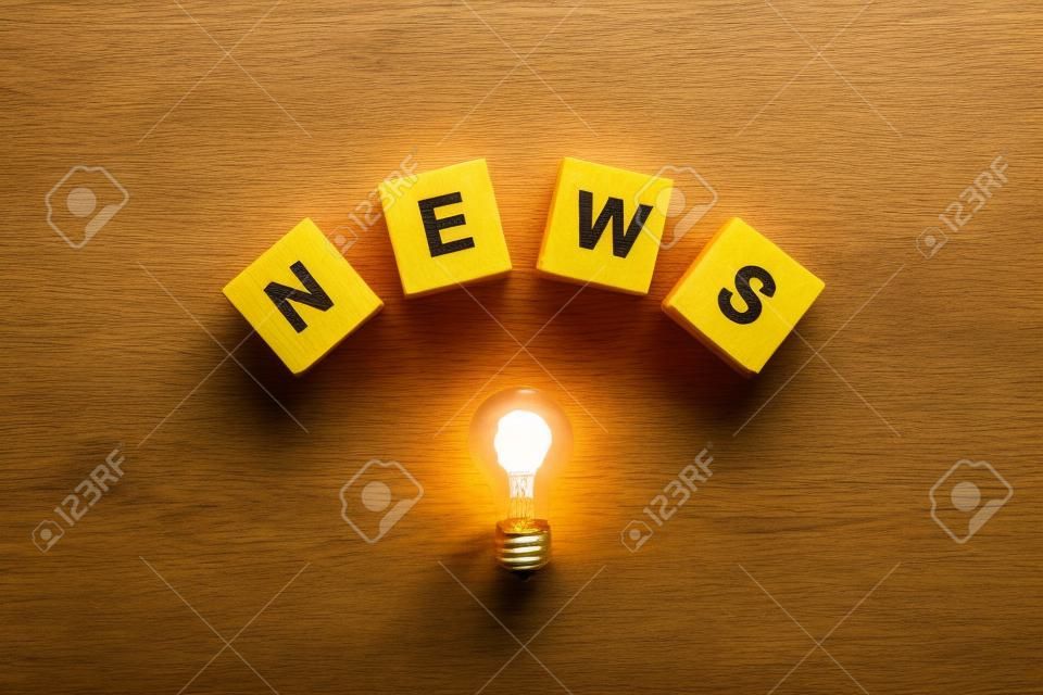 top view of light bulb with wooden cubes with word news on yellow
