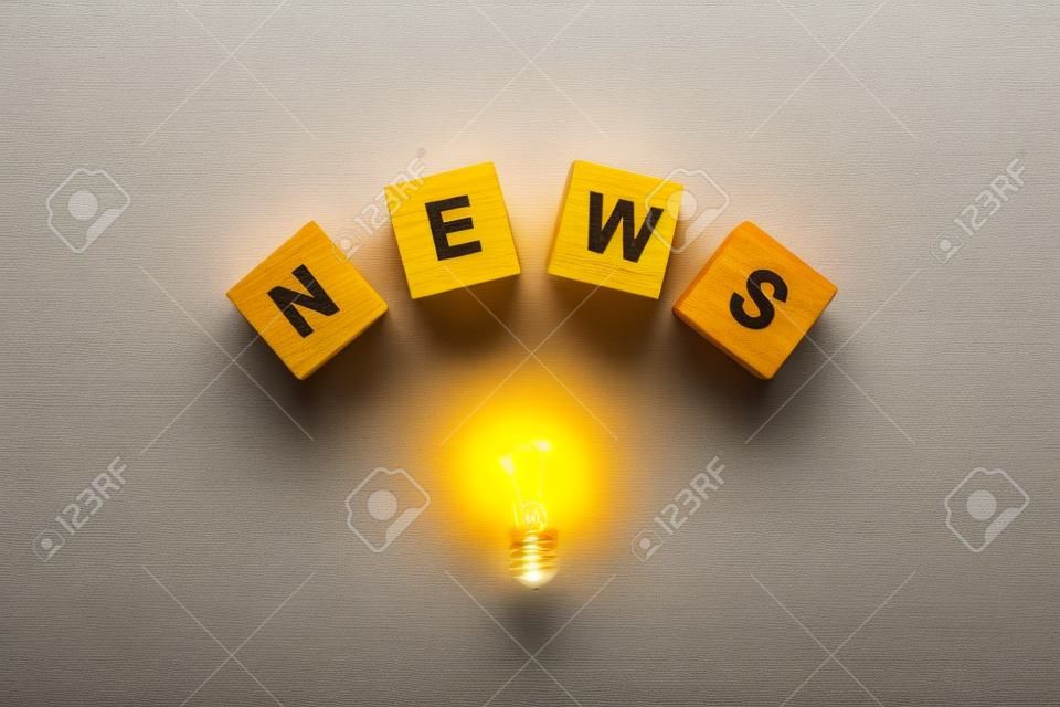 top view of light bulb with wooden cubes with word news on yellow