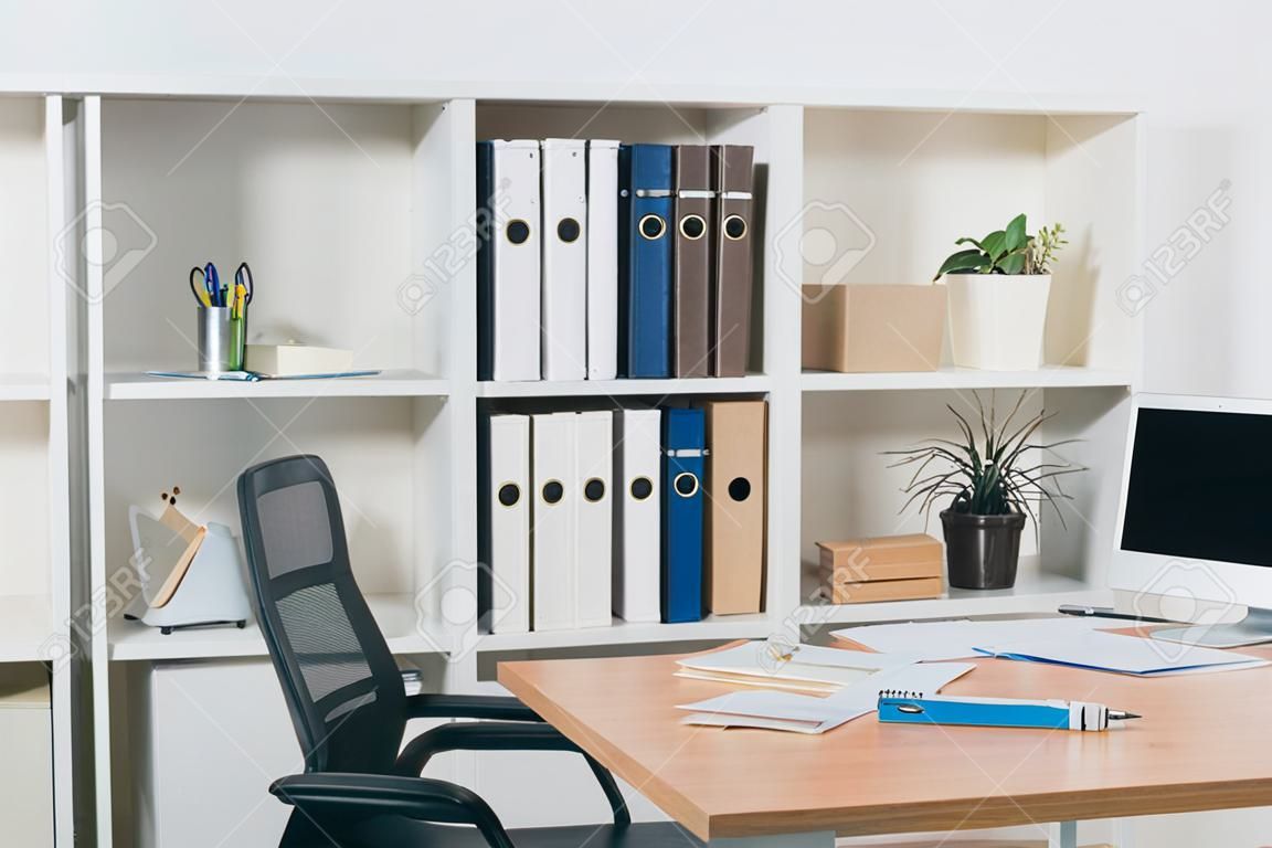 table de bureau avec ordinateur portable, documents, chaises et bibliothèque pour dossiers en arrière-plan