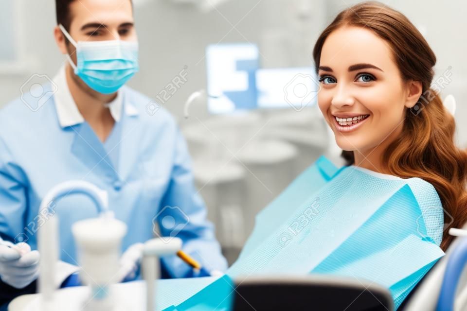 배경에 마스크를 쓴 치과 의사와 함께 웃고 있는 중괄호를 입은 여성의 선택적 초점