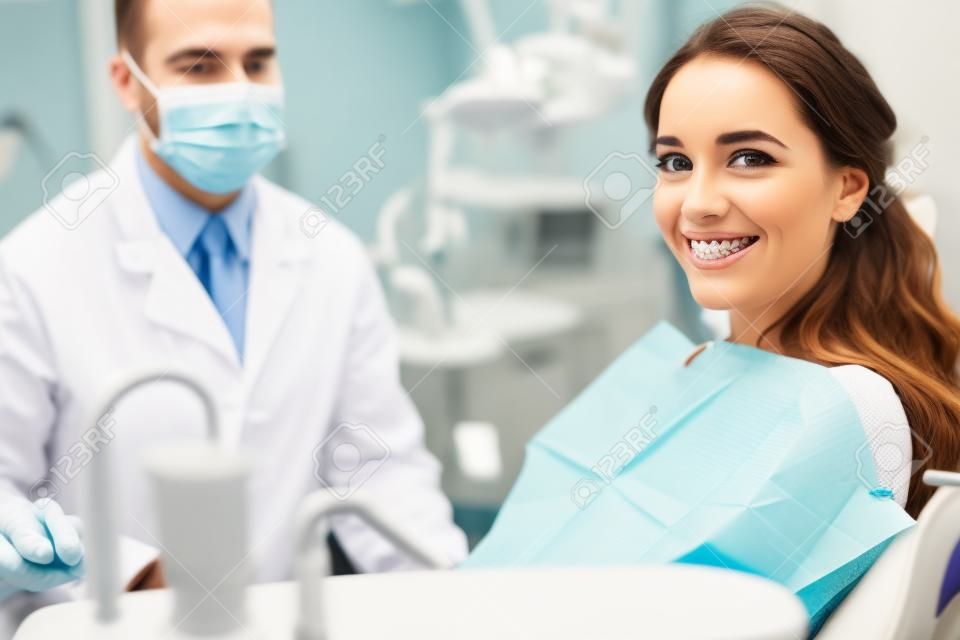 배경에 마스크를 쓴 치과 의사와 함께 웃고 있는 중괄호를 입은 여성의 선택적 초점