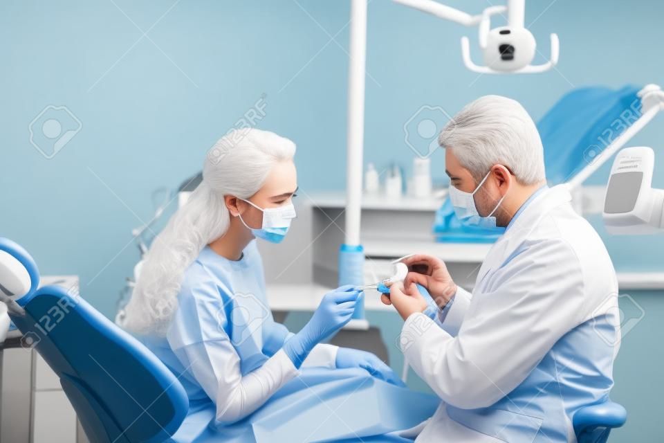dentist in latex gloves and mask holding teeth model near woman