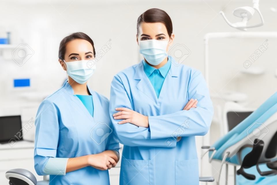 Zahnärztin in Maske, die mit verschränkten Armen in der Zahnklinik neben Kollegin steht