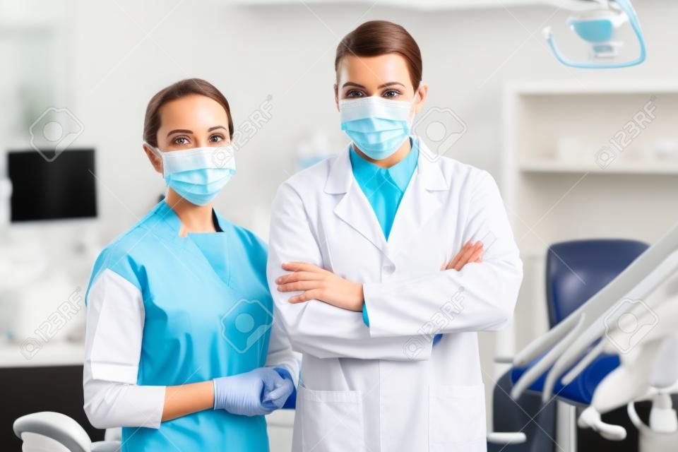 Zahnärztin in Maske, die mit verschränkten Armen in der Zahnklinik neben Kollegin steht