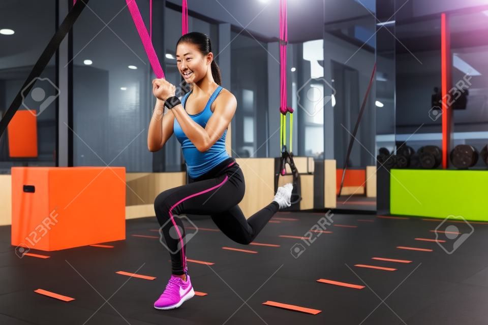 Atlética chica asiática que se extiende con bandas de resistencia en el gimnasio
