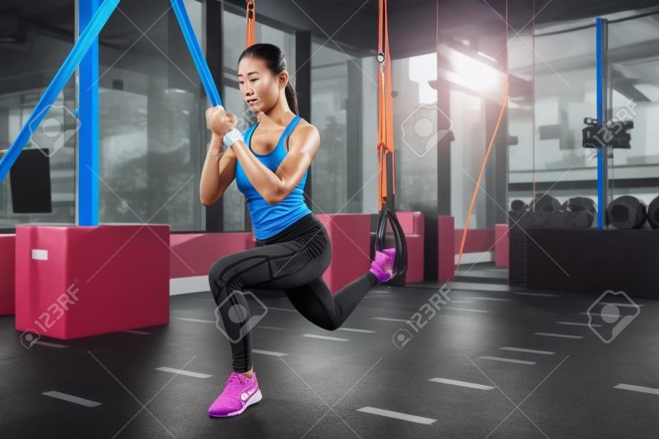 athletic asian girl stretching with resistance bands in fitness center