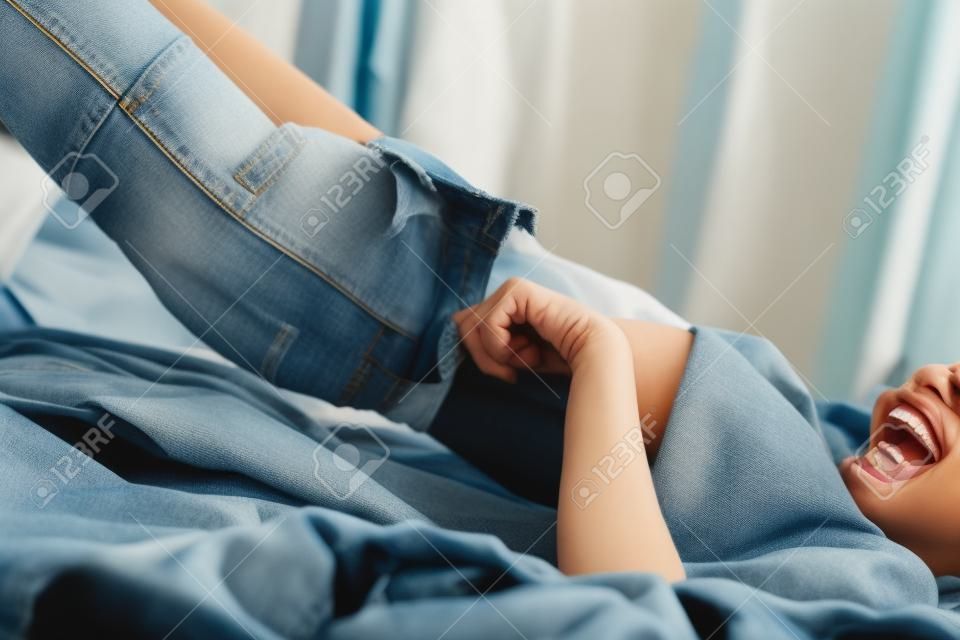 bijgesneden shot van jonge vrouw lachen tijdens het aantrekken van denim broek op bed
