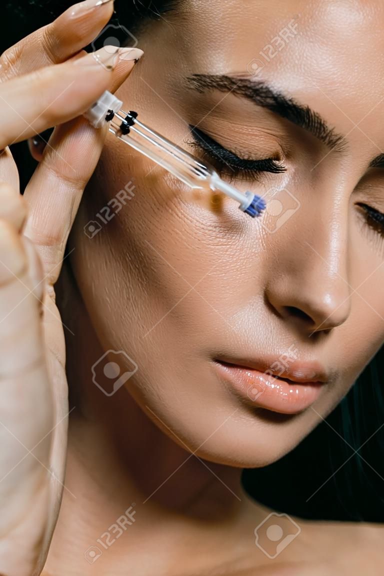 atrakcyjna młoda kobieta nakładająca serum na twarz za pomocą pipety