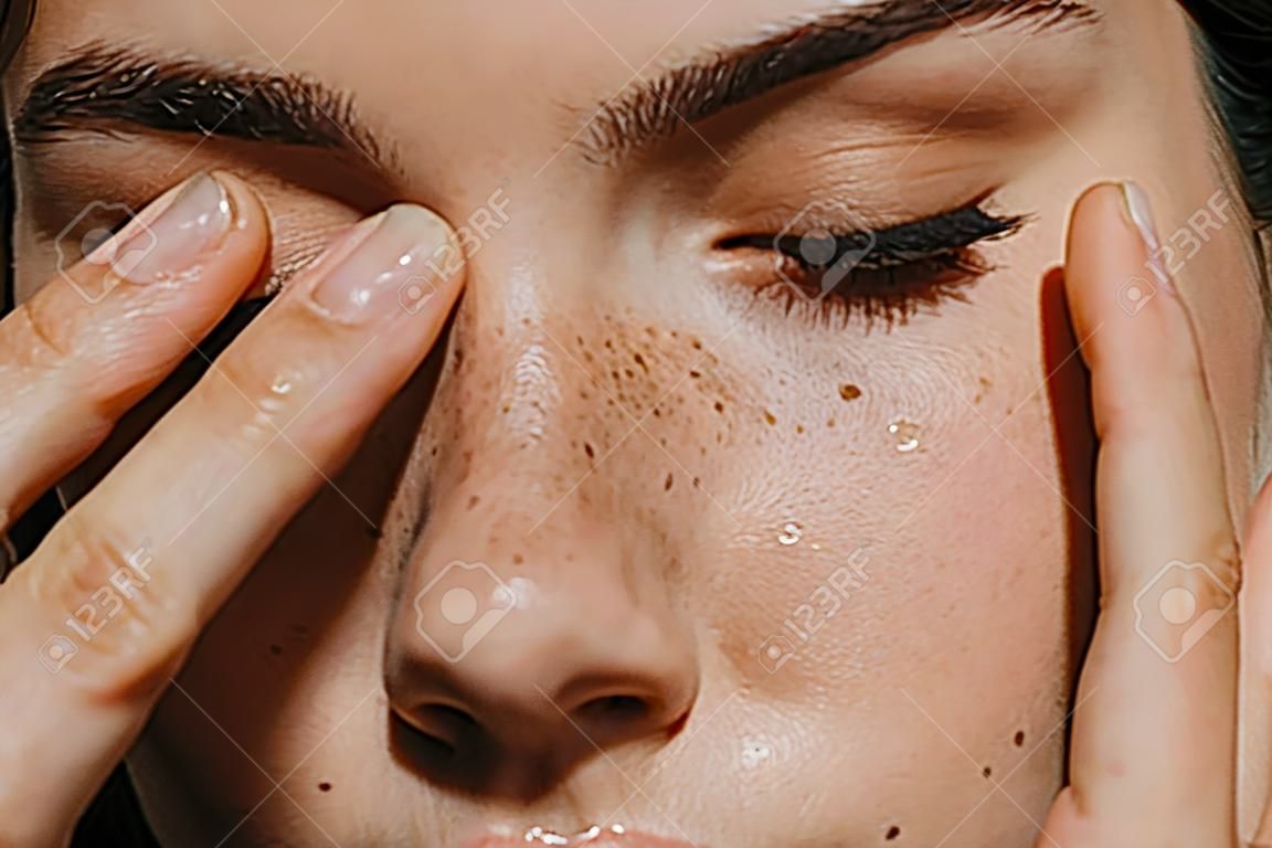 close up view of tender girl with freckles on face touching closed eyes