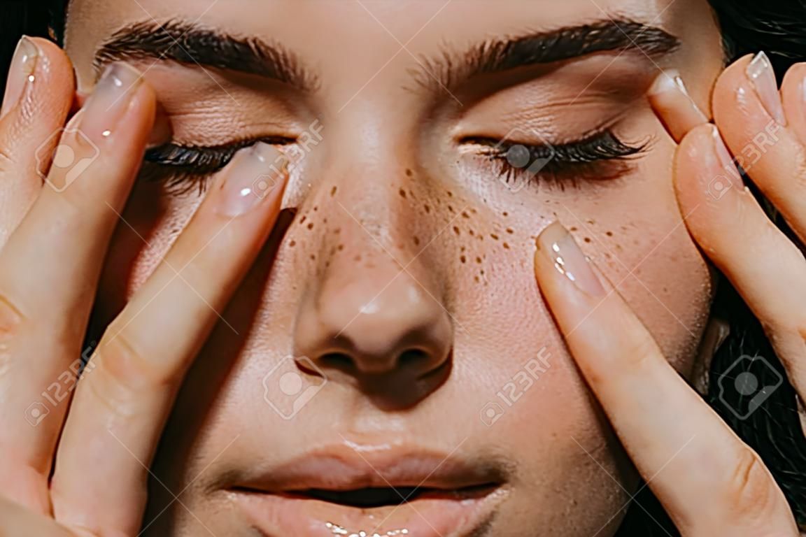 close up view of tender girl with freckles on face touching closed eyes