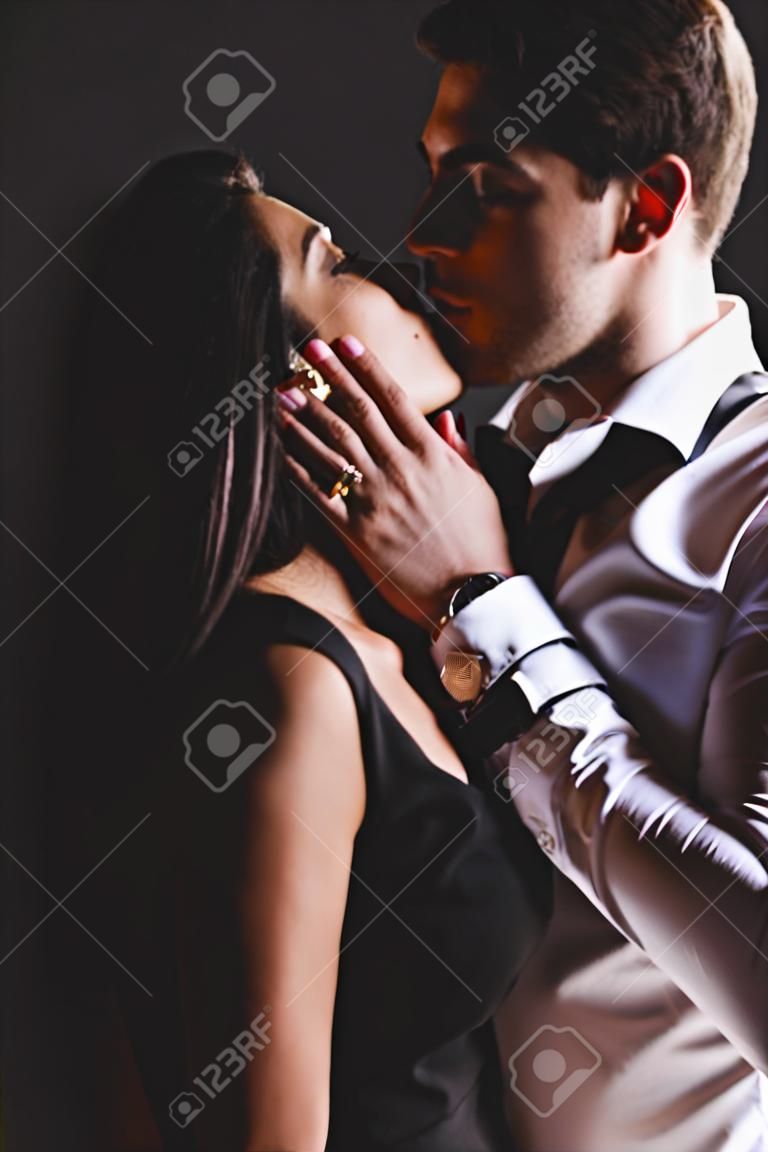 man in white shirt and woman in black dress kissing on black background