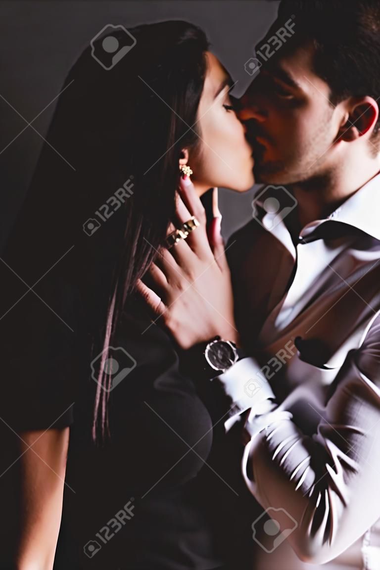uomo in camicia bianca e donna in abito nero che si baciano su sfondo nero