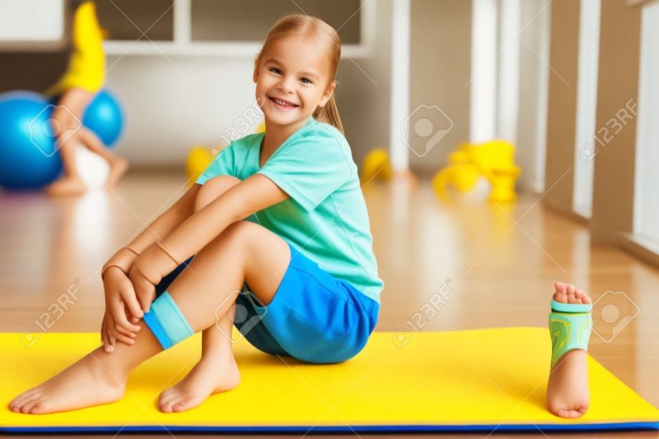 Barefooted kid sitting on yellow fitness mat with smile