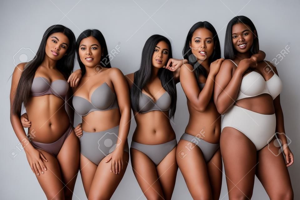 Fünf attraktive junge multiethnische Frauen in Unterwäsche posieren isoliert auf grauem, körperpositivem Konzept vor der Kamera