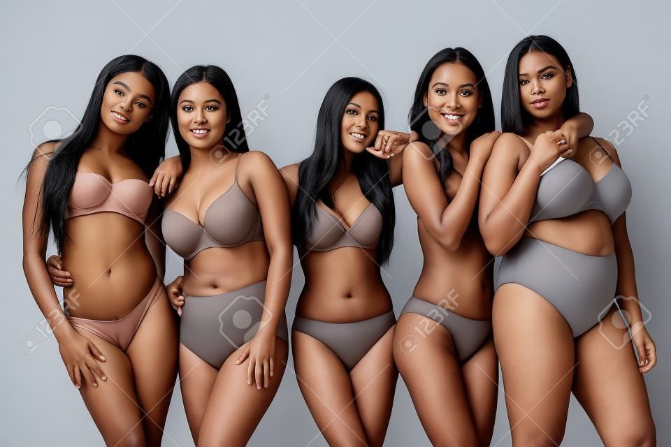 Fünf attraktive junge multiethnische Frauen in Unterwäsche posieren isoliert auf grauem, körperpositivem Konzept vor der Kamera