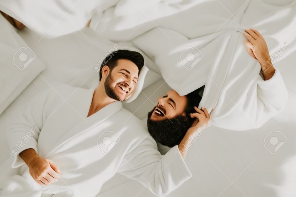 Blick von oben auf ein fröhliches Paar in Bademänteln, das sich beim Liegen auf dem Bett ansieht