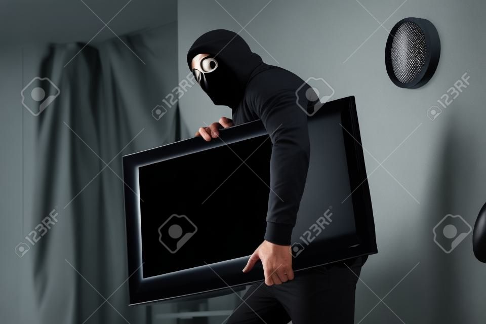 Robber in black mask stealing flat-screen tv with blank screen from apartment