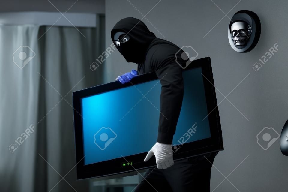 Robber in black mask stealing flat-screen tv with blank screen from apartment