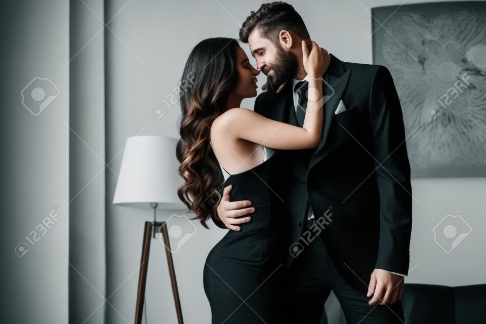 mulher atraente no vestido preto abraçando com homem apaixonado no terno