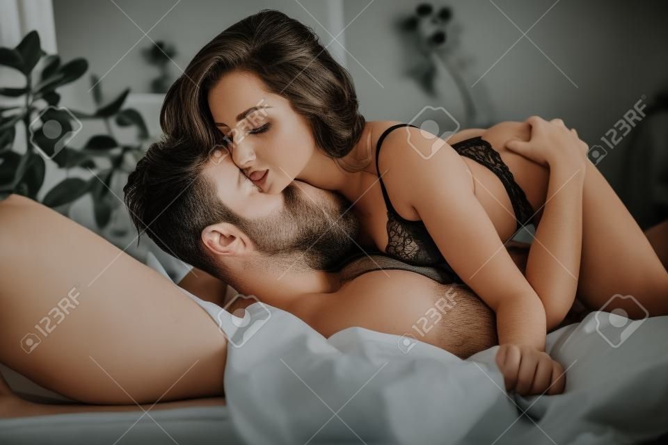 passionate man kissing woman in black underwear on bed