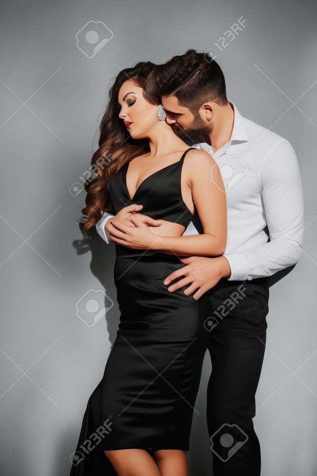 handsome man kissing neck of beautiful woman in black dress on white