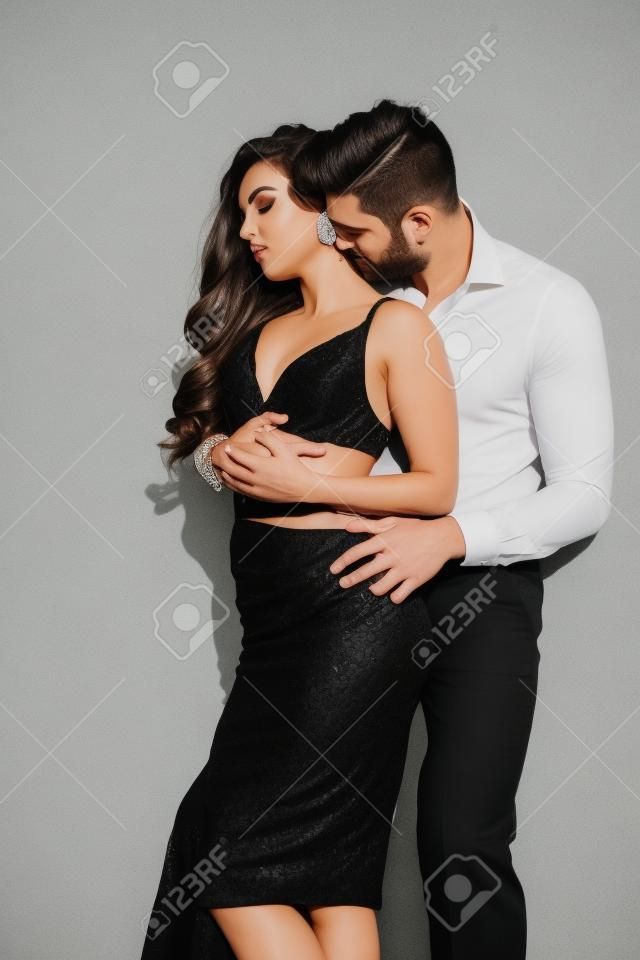 handsome man kissing neck of beautiful woman in black dress on white
