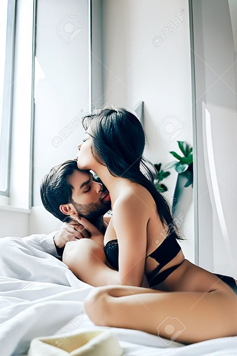 passionate man kissing and undressing brunette girl on bed
