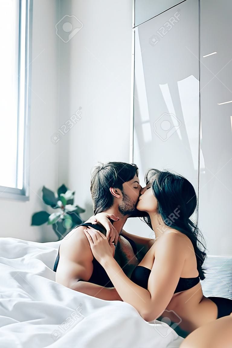 leidenschaftlicher Mann küsst und entkleidet brünettes Mädchen auf dem Bett