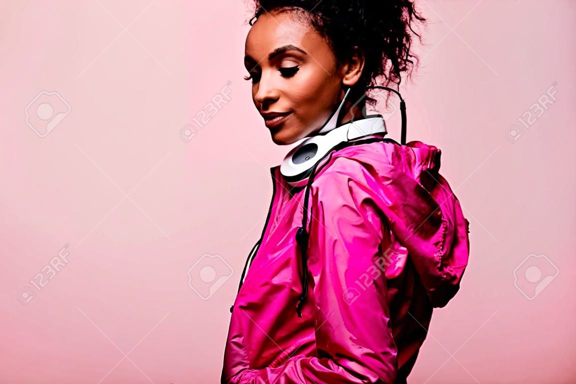 복사공간이 있는 분홍색으로 격리된 헤드폰을 끼고 윈드브레이커를 입은 아름다운 아프리카계 미국인 운동가