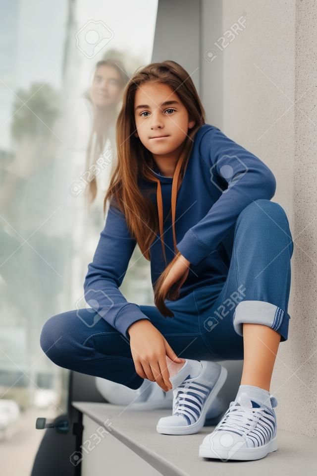 Curious teenager in sneakers sitting on window sill and looking at camera