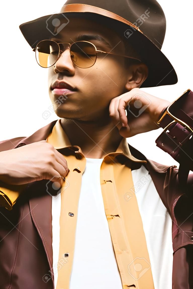 fashionable mixed race man in sunglasses and hat posing with eyes closed isolated on white
