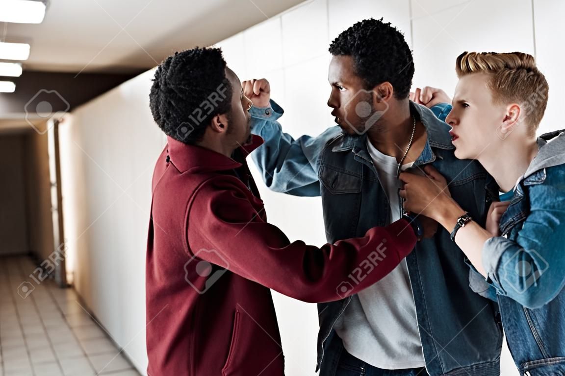 two multiethnic students fighting in corridor in college