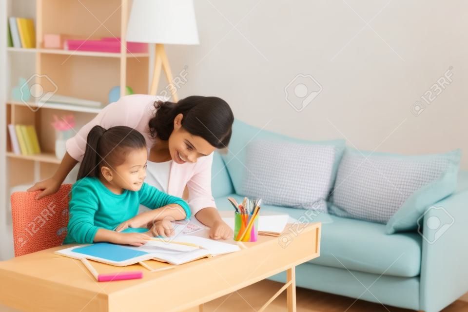 Mulher bonita que ajuda a filha adorável que faz o trabalho escolar em casa