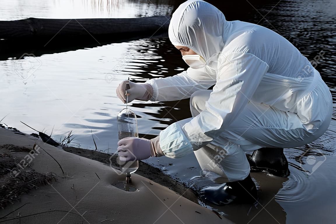 water inspector in protective costume and respirator taking water sample at river