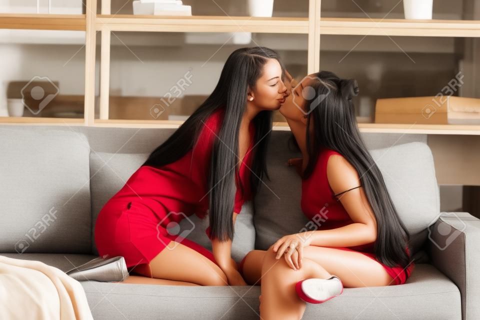 Dos lesbianas besándose mientras está sentado en el sofá en la sala de estar