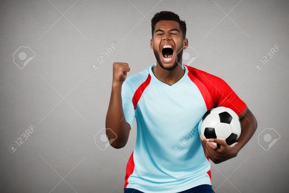 Jugador de fútbol emocionado con balón y mano apretada gritando aislado en blanco