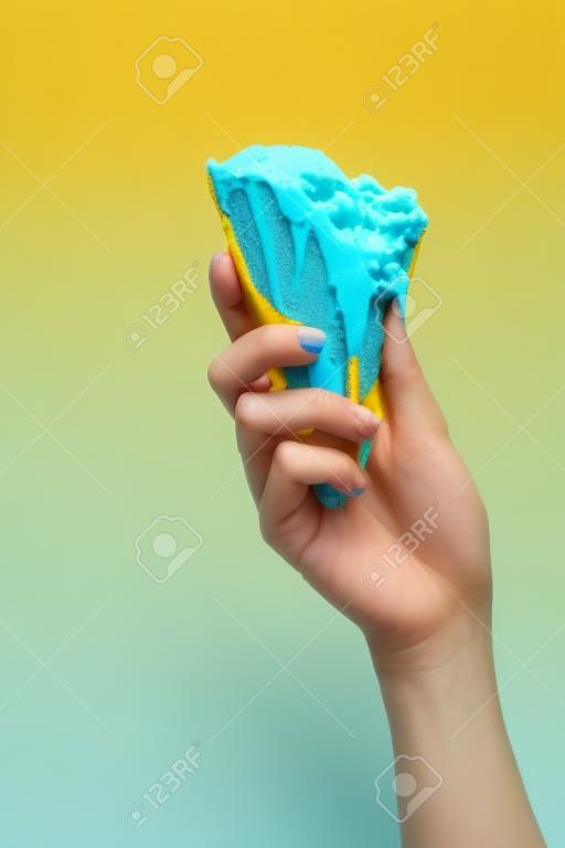 노란색으로 분리된 바삭한 와플 콘에 맛있는 녹은 파란색 아이스크림을 들고 있는 여성의 부분적인 모습