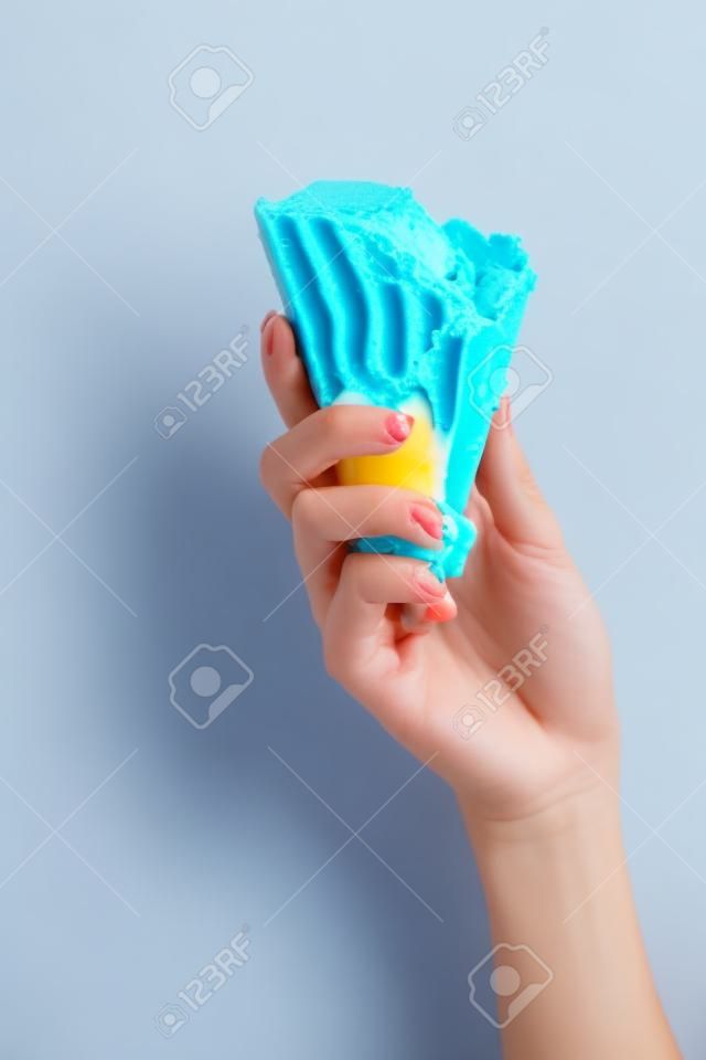 Vista parcial de la mujer sosteniendo delicioso helado azul derretido en cono de waffle crujiente aislado en amarillo