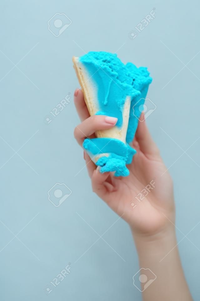 노란색으로 분리된 바삭한 와플 콘에 맛있는 녹은 파란색 아이스크림을 들고 있는 여성의 부분적인 모습