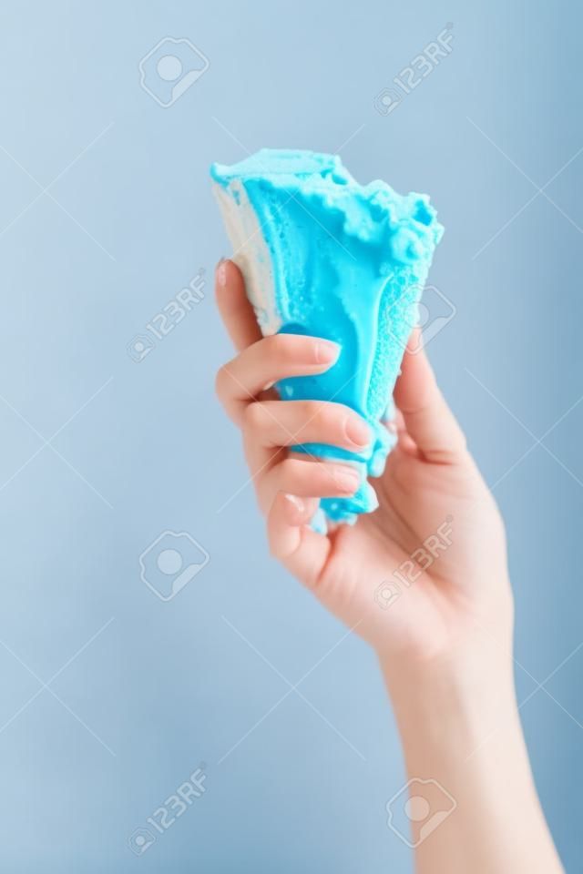 gedeeltelijk uitzicht op vrouw houden heerlijk gesmolten blauw ijs in knapperige wafel kegel geïsoleerd op geel