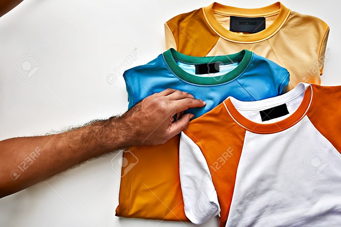cropped view of man holding ochre t-short near beige, orange, turquoise and blue ones on white background