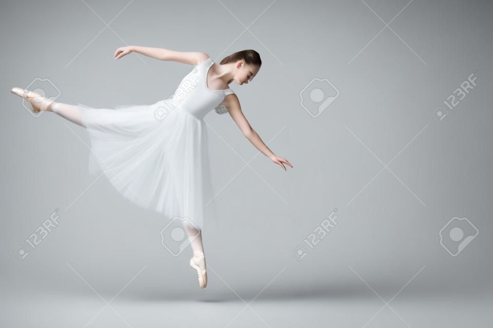 aantrekkelijke jonge ballerina dansen in witte jurk op grijze achtergrond